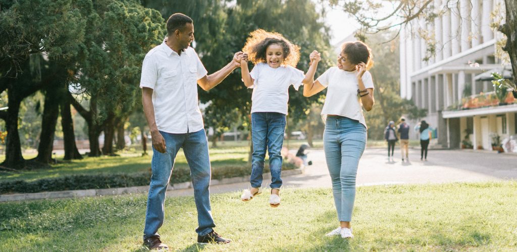 Mother and father helping their daughter jump while in the park.