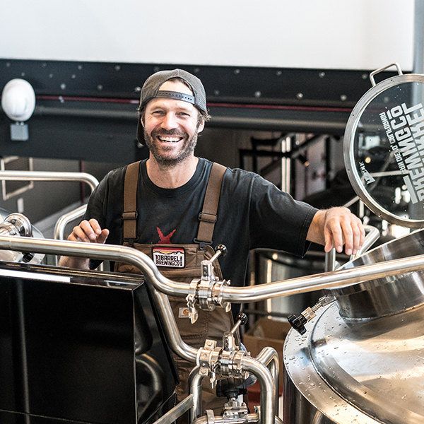 Brewery business owner smiling while standing with equipment.
