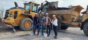 four team members holding shovels by construction equipment