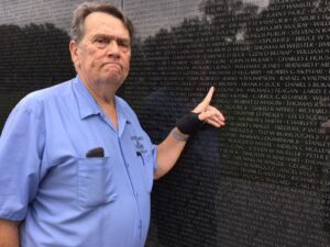 Gil, proud veteran  pointing at a wall with names on it for Vietnam vets