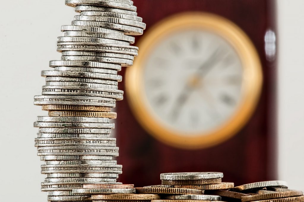 Stack of coins on a table with clock in the background.