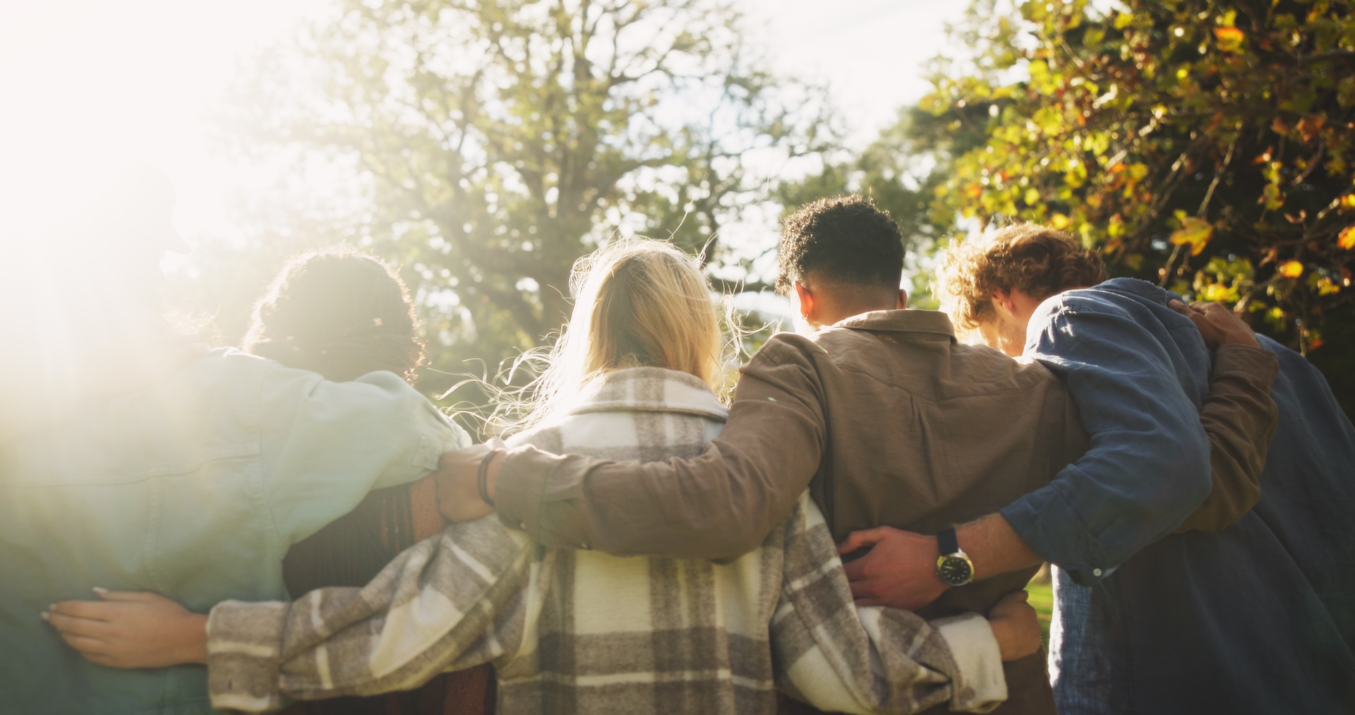 Photo of people linked together with their arms with foliage in the background